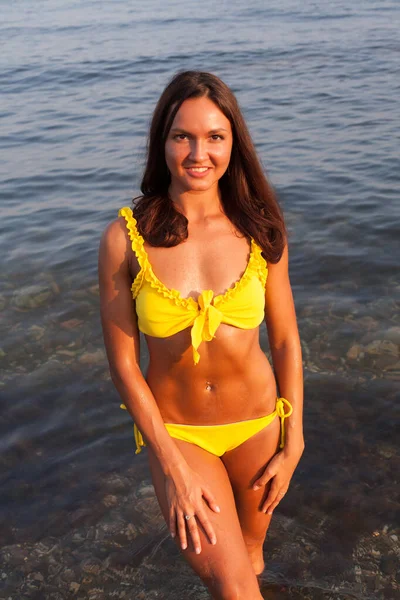 Hermosa mujer con el pelo largo en traje de baño amarillo toma el sol en una playa de mar — Foto de Stock