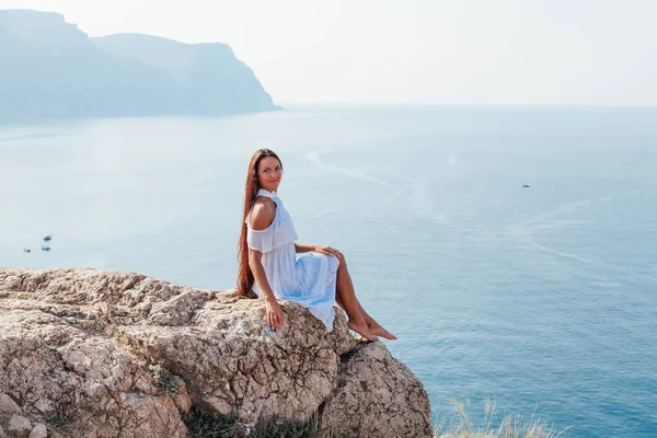 Beautiful woman with long hair in dress on cliff cliff by the sea — Stock Photo, Image