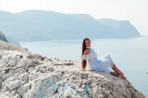 Beautiful woman with long hair in dress on cliff cliff by the sea — Stock Photo, Image