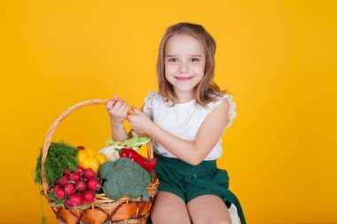 Küçük kız bir sepet olgun sebze tutuyor.