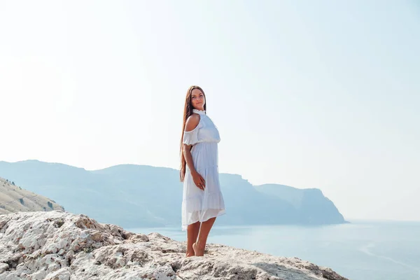 Beautiful woman with long hair in dress on cliff cliff by the sea — Stock Photo, Image