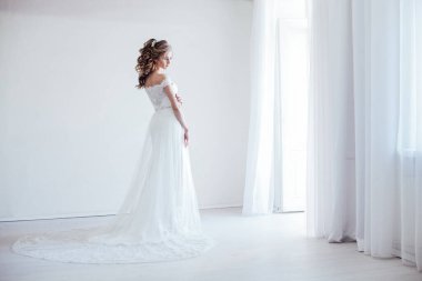 Gelin beyaz bir odada gelinlik giyiyor.
