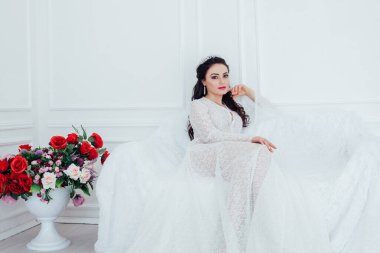 Gelinlik giymiş gelin beyaz bir kanepede oturuyor.
