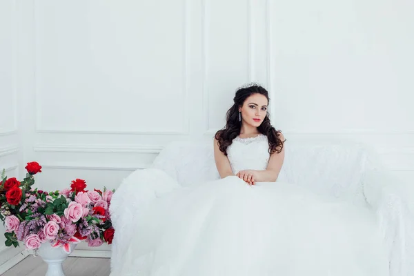 Bride in a wedding dress and a crown sits in the white hall — Stock Photo, Image