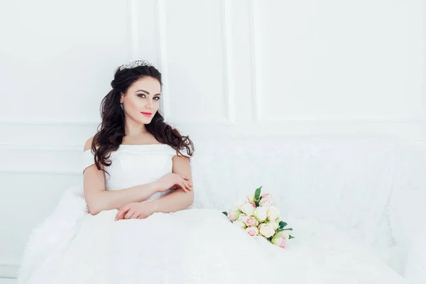 Nevěsta ve svatebních šatech sedí na pohovce svatební kytice — Stock fotografie