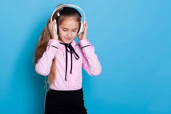Dívka poslouchá hudbu ve velkých sluchátkách a tance na modrém pozadí — Stock fotografie