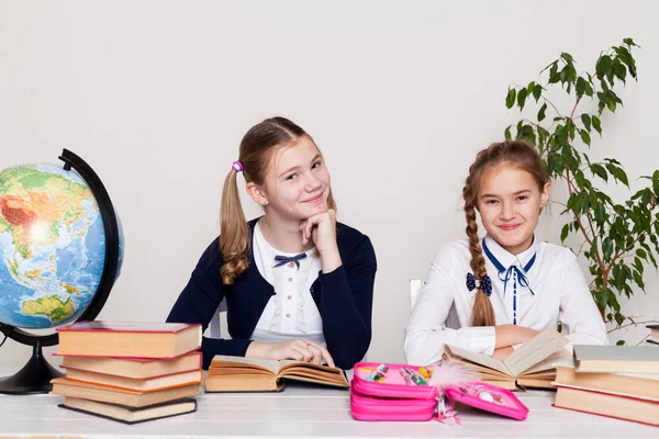 Two girls of the school with books for studying sit at the desk in the classroom — Stock Photo, Image