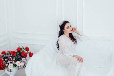 Gelinlik giymiş gelin beyaz bir kanepede oturuyor.