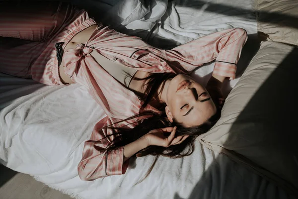 Брюнетка в розовом пижаме лежит на кровати — стоковое фото