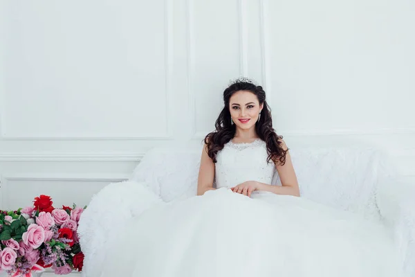 Braut in Brautkleid und Krone sitzt im weißen Saal — Stockfoto