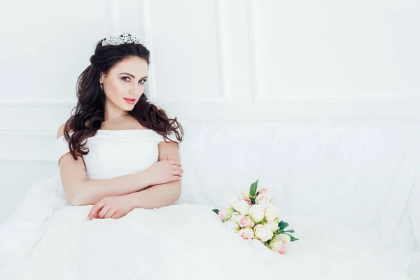 Nevěsta ve svatebních šatech sedí na pohovce svatební kytice — Stock fotografie