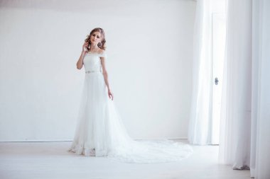 Gelin beyaz bir odada gelinlik giyiyor.