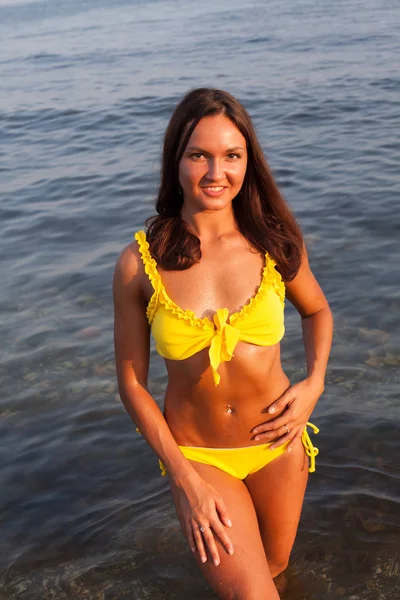 Hermosa mujer con el pelo largo en un traje de baño amarillo camina por la playa junto al mar — Foto de Stock