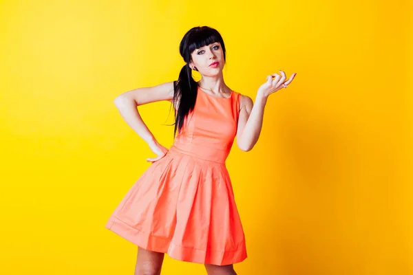 Girl in orange dress on a yellow background hands up — Stock Photo, Image