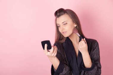 Ceketli kız aynada fırça makyajı yapıyor.