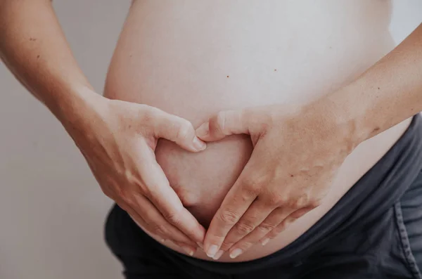 Der Magen einer schwangeren Frau und die Hände Glücksherz — Stockfoto