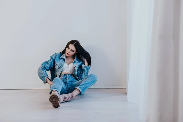 Menina bonita em jeans roupas sentadas no chão em uma sala branca — Fotografia de Stock