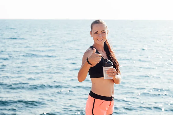 Chica beber agua de un agitador después de un entrenamiento en la playa — Foto de Stock