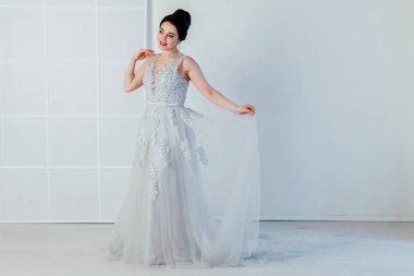 Gelin beyaz odada gelinlik giymiş.