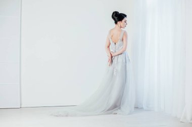 Gelin beyaz odada gelinlik giymiş.