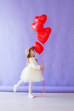 Kalp şeklinde kırmızı balonları olan güzel küçük bir kız.