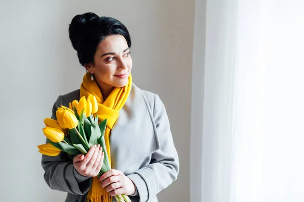 Mulher morena em casacos com tulipas amarelas — Fotografia de Stock