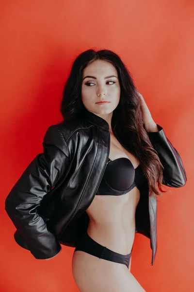 Chica morena en chaqueta de cuero y lencería negra sobre un fondo rojo — Foto de Stock