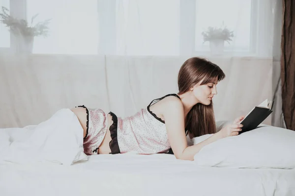 Lány olvas egy könyvet a pizsama feküdt fehér ágyban — Stock Fotó