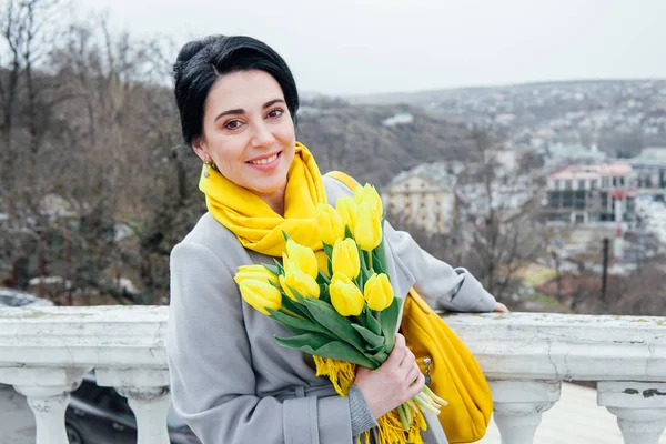 Mulher morena em casacos com tulipas amarelas — Fotografia de Stock