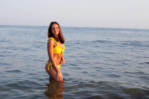 Beautiful woman with long hair in yellow swimsuit sunbathes on the beach by the sea — 스톡 사진