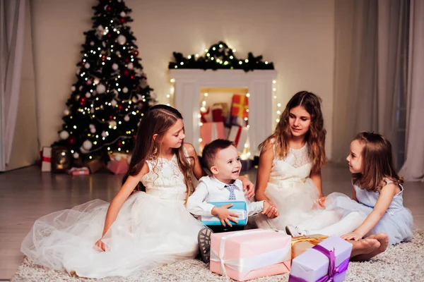 O menino e três meninas abrir presentes árvore de Natal ano novo grinalda — Fotografia de Stock