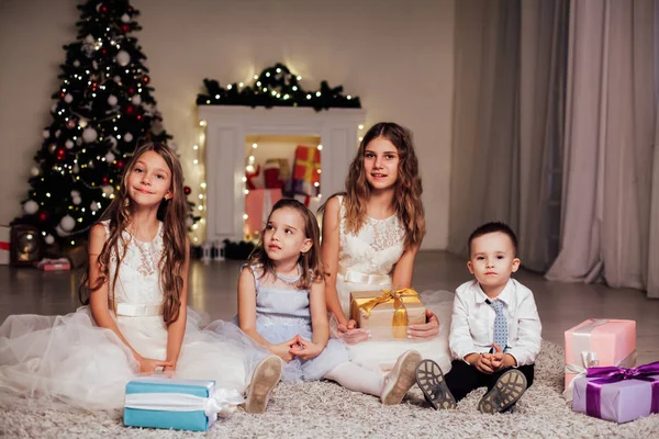 O menino e três meninas abrir presentes árvore de Natal ano novo grinalda — Fotografia de Stock