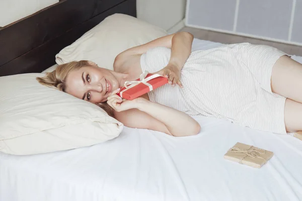 Portret van een mooie blonde vrouw cadeau op het bed in de slaapkamer — Stockfoto