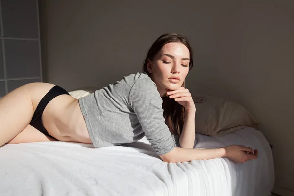 Morena mujer en ropa interior se encuentra en la cama en el dormitorio —  Fotos de Stock
