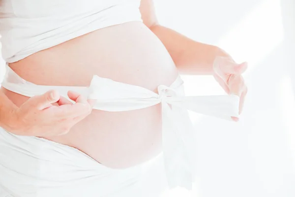 Schwangerer Bauch und weiße Schleife als Geschenk — Stockfoto