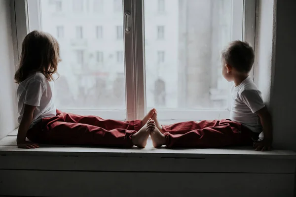 Junge und Mädchen sitzen auf der Fensterbank und schauen aus dem Fenster — Stockfoto