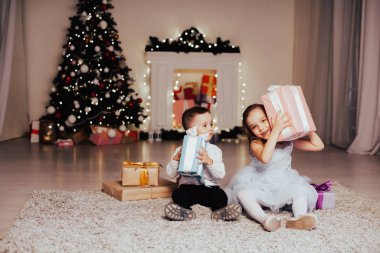 Erkek ve kız çocukları yeni yıl hediyelerini açar Noel ışıkları Noel ağacı çelenkleri
