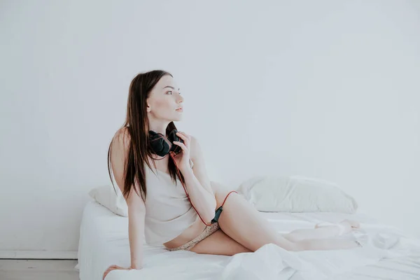 Žena v pyžamu poslechu hudby se sluchátky na posteli — Stock fotografie