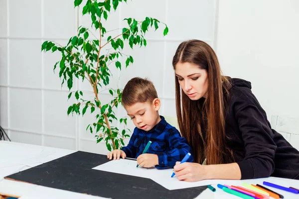 Мама учит маленького мальчика рисовать маркеры за столом — стоковое фото