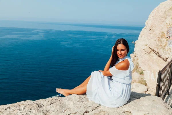 Beautiful woman in dress looks at the sea view from a cliff — Stock Photo, Image