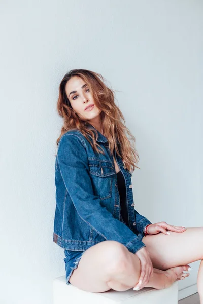 Portrait d'une belle femme à la mode dans une veste en denim et un short à un mur blanc — Photo