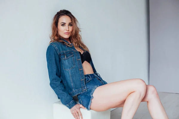 Portrait d'une belle femme à la mode dans une veste en denim et un short à un mur blanc — Photo