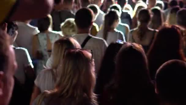 사람들은 밤에 콘서트에서 음악에 맞춰 춤추는 사람들 뒤에서 — 비디오