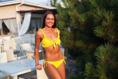 Sarı mayolu, uzun saçlı güzel bir kadın deniz kenarında yürüyor.