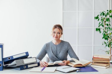 Ofiste kitap ve belgelerle dolu bir masada bir iş kadınının portresi.