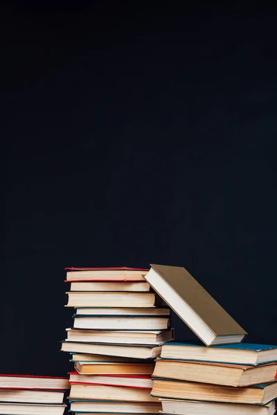 Molti pile di libri educativi per esami universitari in biblioteca su uno sfondo nero — Foto Stock