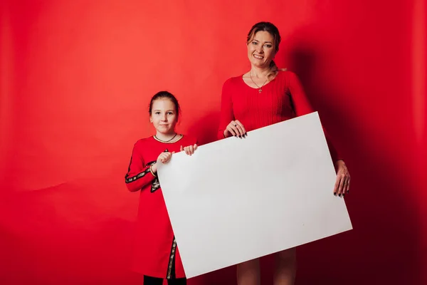 Portrait with a daughter with mother a sign for inscriptions on a red background — Stock Photo, Image