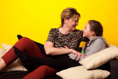 Güzel bir kız ve Wjman siyah bir kanepede uzanır. Yastıklı ev yapımı giysiler içinde.