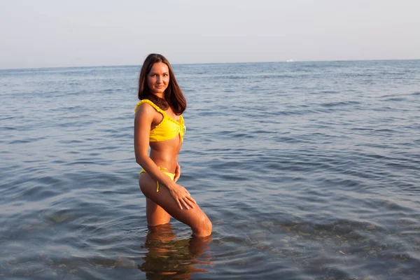 Schöne gebräunte Frau im gelben Badeanzug sonnt sich am Strand am Meer — Stockfoto