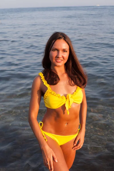 Krásná opálená žena ve žlutých plavkách se opaluje na pláži u moře — Stock fotografie